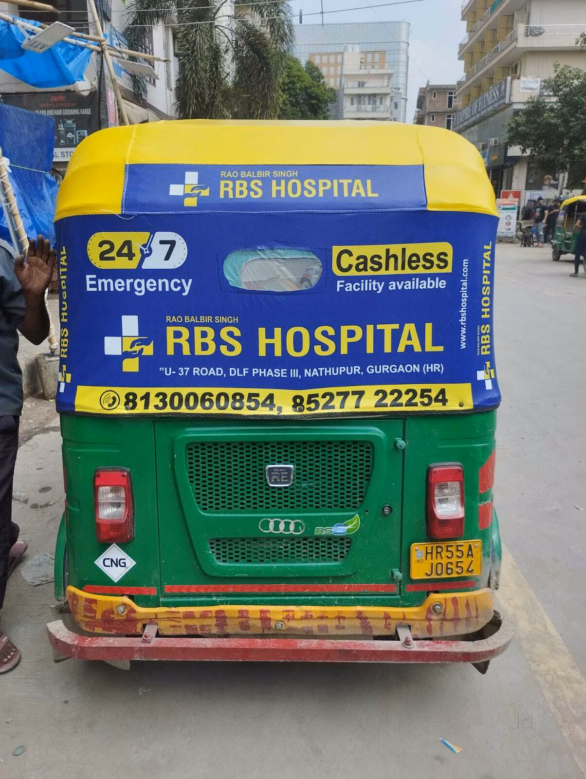 A colorful auto rickshaw wrapped with eye-catching ads driving through a busy street in Delhi with city landmarks visible
